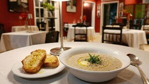 Ein Esstisch mit einer Suppenschüssel, geröstetem Brot, einem Löffel und einer Kerze.