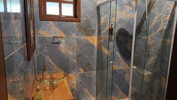 Een badkamer met een douche met glazen wand, een houten wastafelmeubel met een wasbak van glas en een raam boven de wasbak.