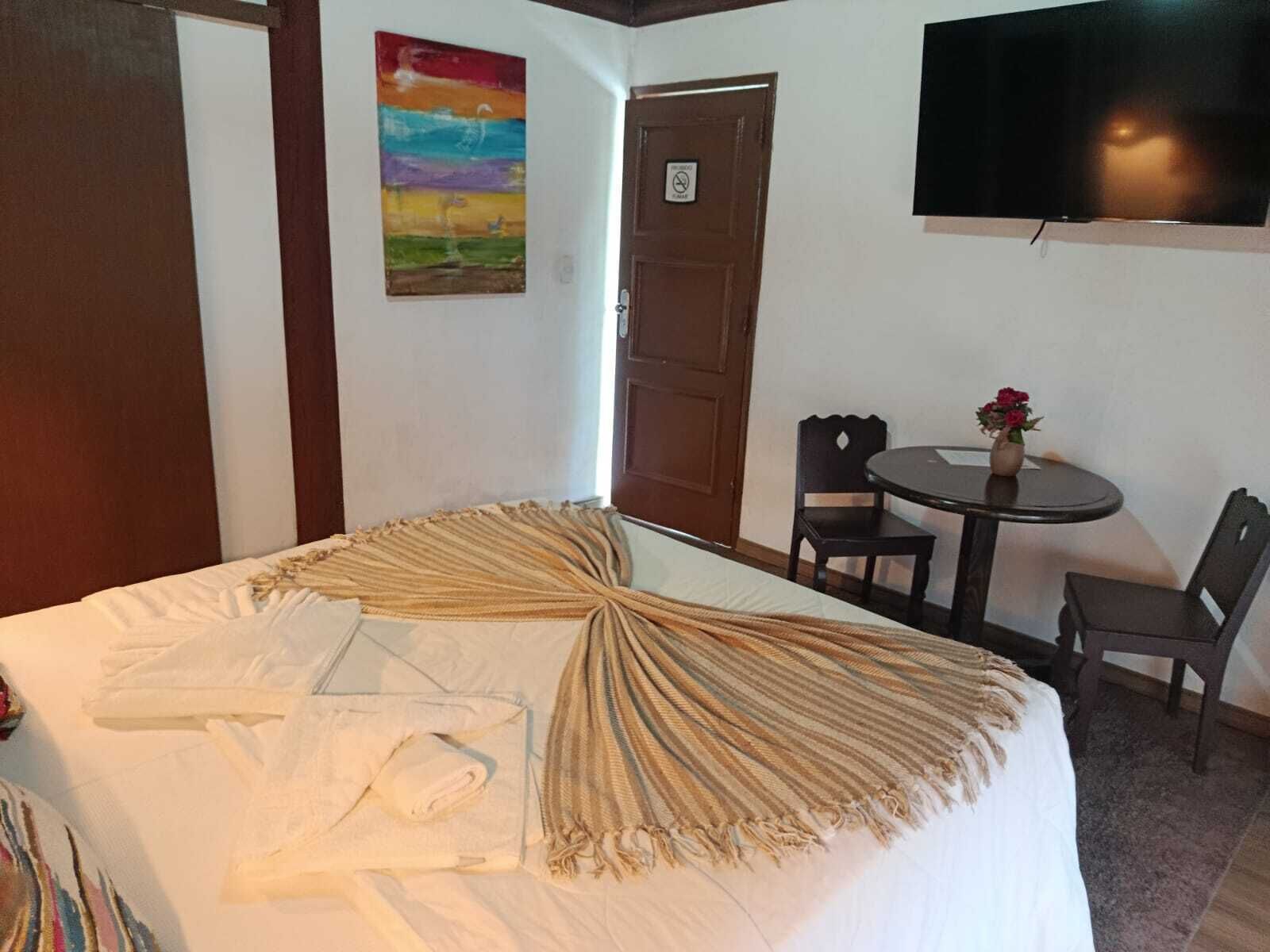Una habitación de hotel con cama, televisor, una mesita con sillas y una puerta.