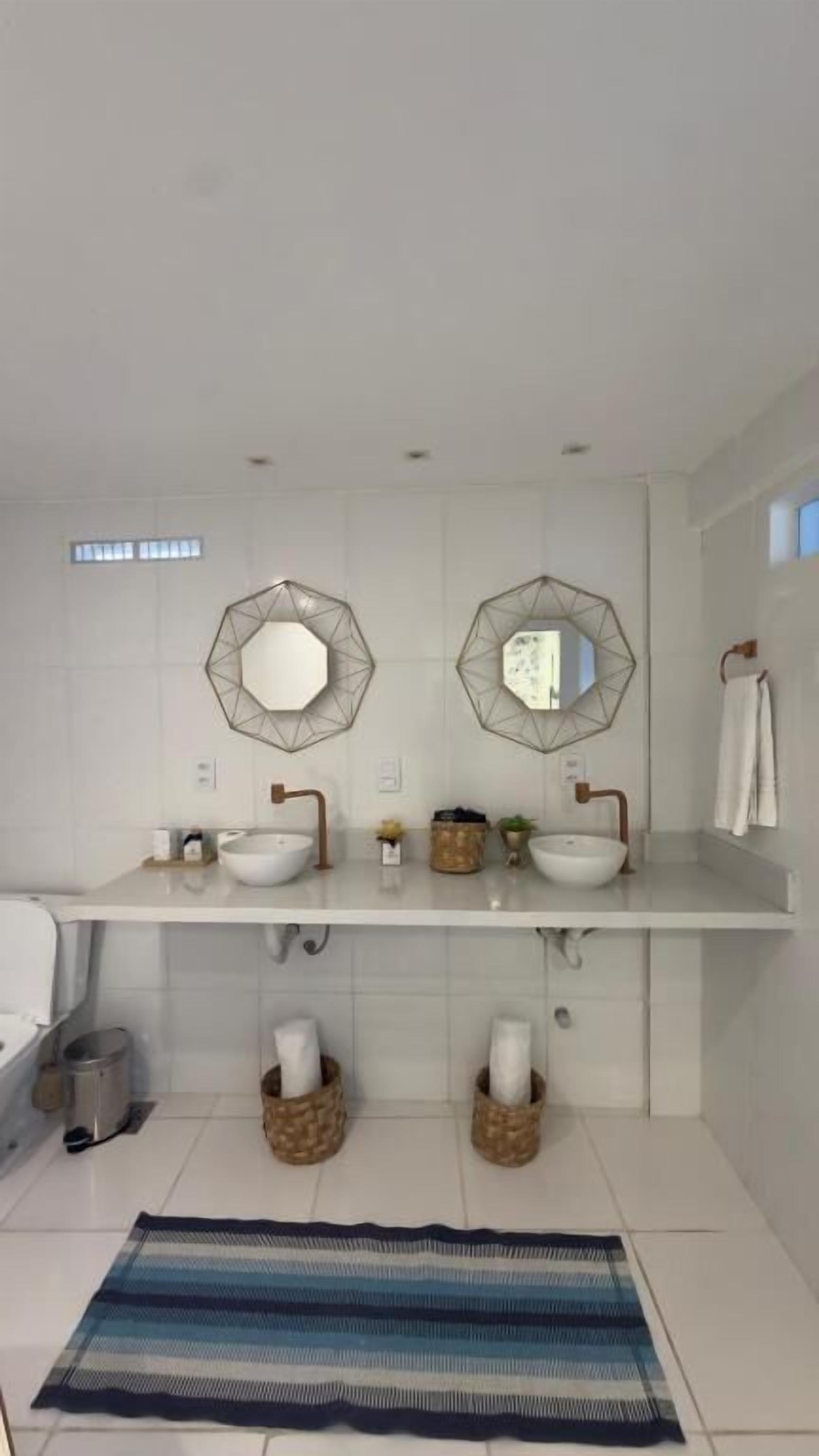 A modern bathroom with two sinks, geometric mirrors, and a striped rug.