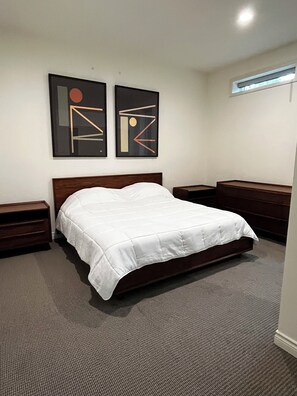 Ein Schlafzimmer mit einem Bett, zwei Nachttischen, einer Kommode und abstrakten Wandbildern.