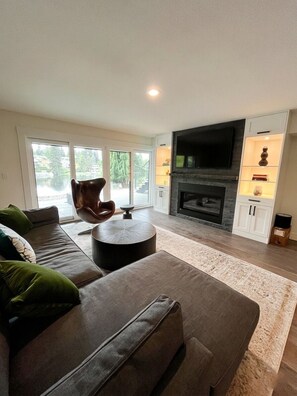 A modern living room with a large sofa, a round coffee table, a fireplace, and a television. - Sun-Drenched 5BR Shoreline Haven with Lake Access (Normandy Park)