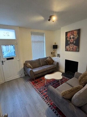 Ein Wohnzimmer mit einer Couch, einem Couchtisch, einem gemusterten Teppich, einem Gemälde und einem Kamin.