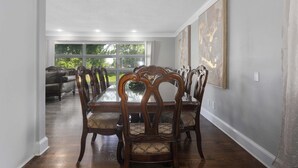 A dining area with a long wooden table and chairs, a window with a view of greenery, and a painting on the wall. - Great Home_Sleeps10_ Large Yard_Room for Everyone (Overland Park)