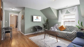 Ein Wohnzimmer mit einer Couch, einem Sessel, einem Couchtisch und einem an der Wand befestigten Fernseher.