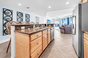 A modern kitchen with granite countertops, wooden cabinets, and a large island. - Palazzo 908 (Panama City Beach)