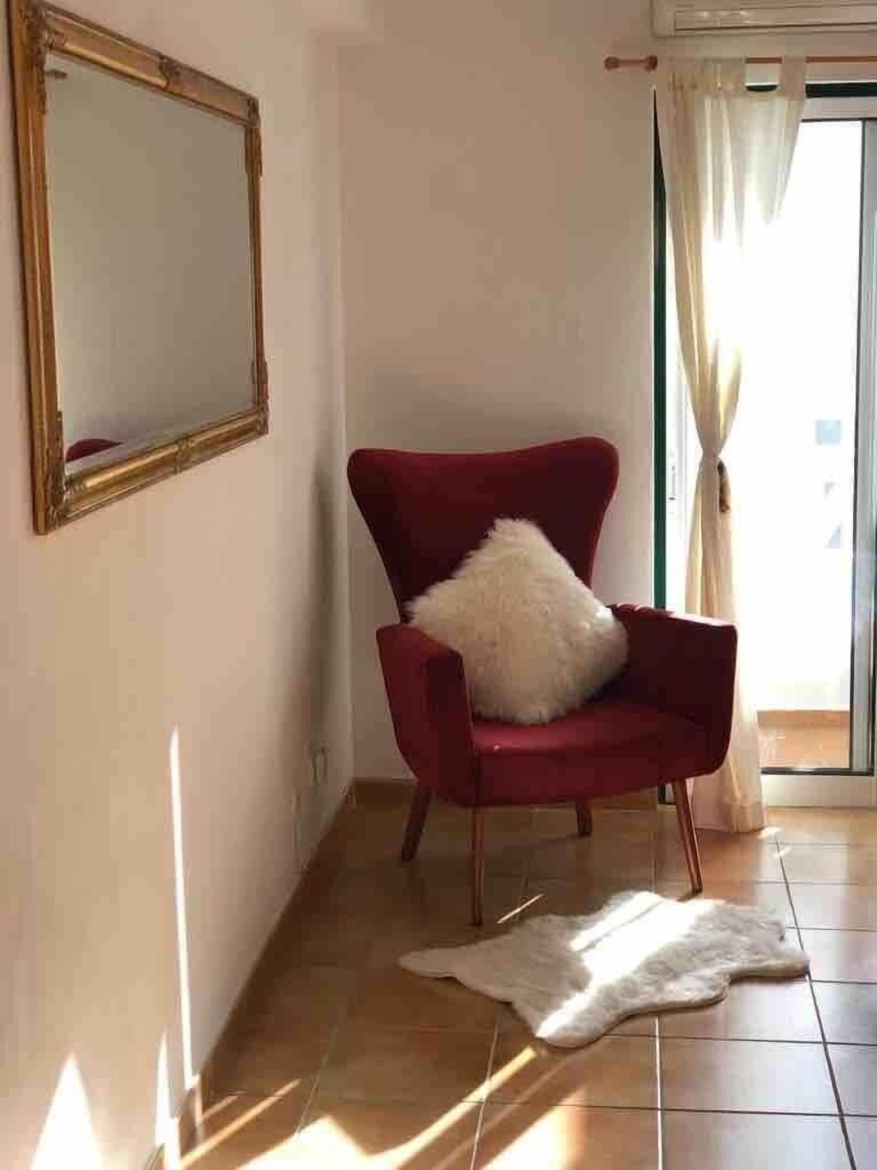Habitació amb una cadira vermella, un coixí blanc i esponjós, una catifa blanca i un mirall gran a la paret.