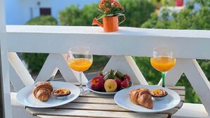 Ein Balkon mit einem für das Frühstück gedeckten Tisch, mit Croissants, Obst und Orangensaftgläsern.