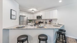 A modern kitchen with white cabinets, stainless steel appliances, granite countertops, and bar stools. - Lakefront living with stunning views and easy pool access, Open-concept space,Close to everything (Lake Ozark)