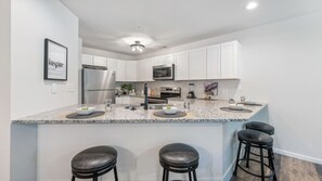 A modern kitchen with white cabinets, stainless steel appliances, granite countertops, and bar stools. - Lakefront living with stunning views and easy pool access, Open-concept space,Close to everything (Lake Ozark)