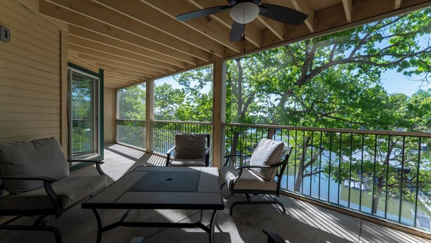 A covered outdoor area with a table and chairs, a ceiling fan, and a view of trees and water. - Lakefront living with stunning views and easy pool access, Open-concept space,Close to everything (Lake Ozark)
