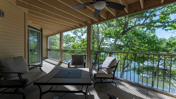 A covered outdoor area with a table and chairs, a ceiling fan, and a view of trees and water. - Lakefront living with stunning views and easy pool access, Open-concept space,Close to everything (Lake Ozark)