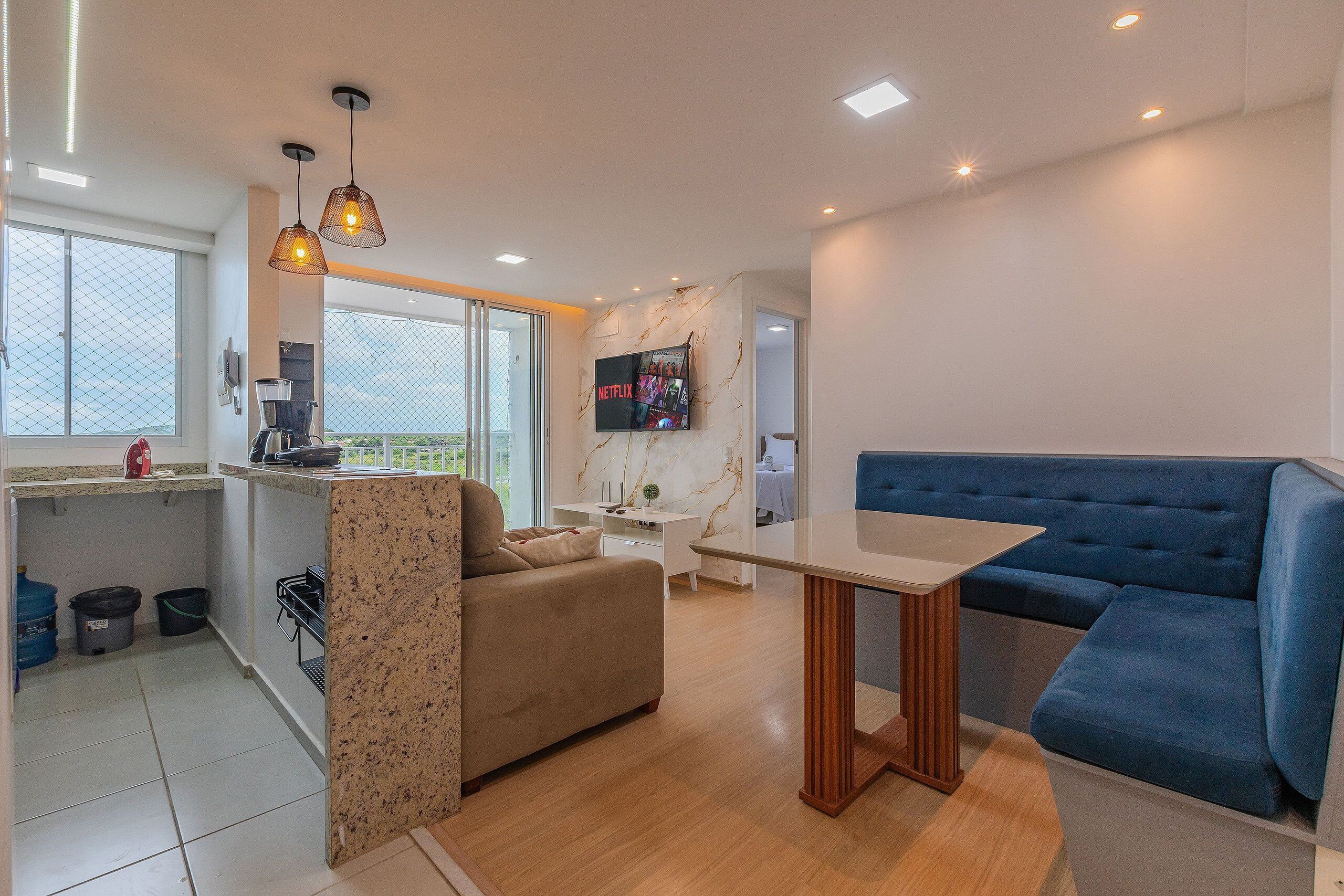 A modern living space with a kitchen, a sofa, a dining table, and a TV mounted on the wall.