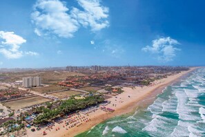 Vista aérea de uma cidade costeira com uma praia extensa, edifícios altos e céu claro.