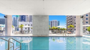 Ein Dachpool mit Liegestühlen und Sonnenschirmen, umgeben von Hochhäusern.