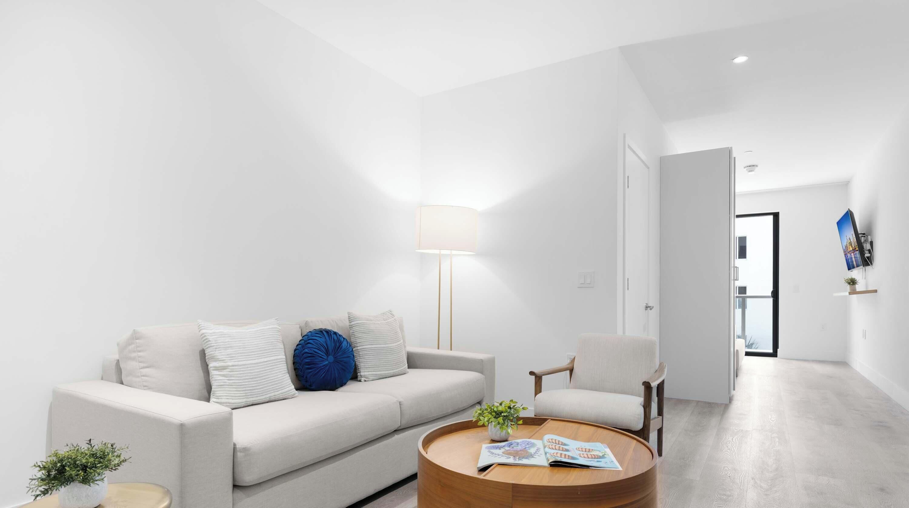 Ein modernes Wohnzimmer mit Sofa, Sesseln, Couchtisch, Lampe und einem flachbildfernseher an der Wand.