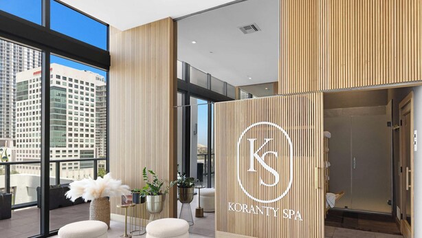 Een modern spa-interieur met een groot logo, potplanten en uitzicht op een stadsbeeld.
