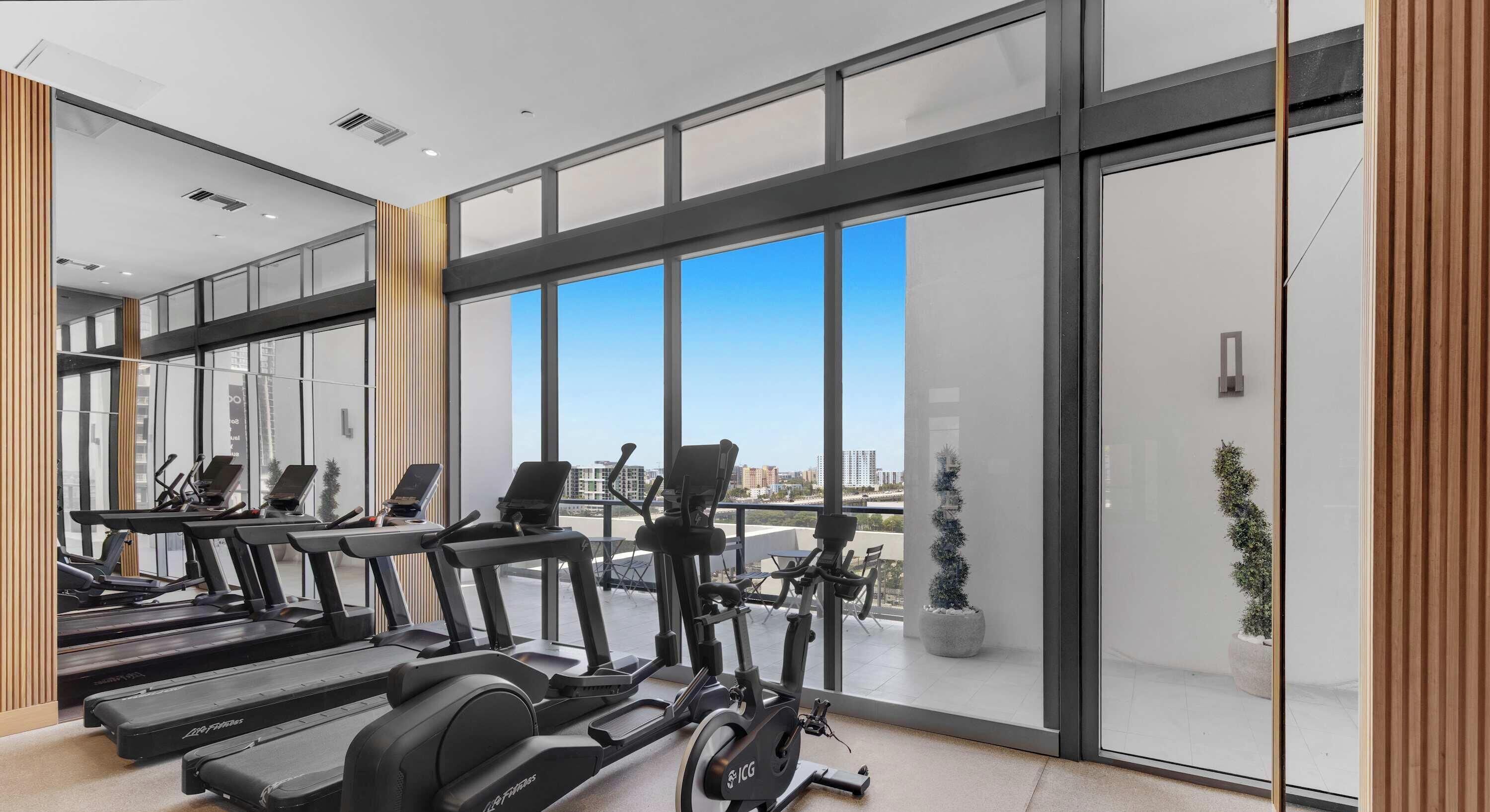 A modern gym with treadmills, stationary bikes, and elliptical machines, large windows with a city view, and a clean, minimalist design.