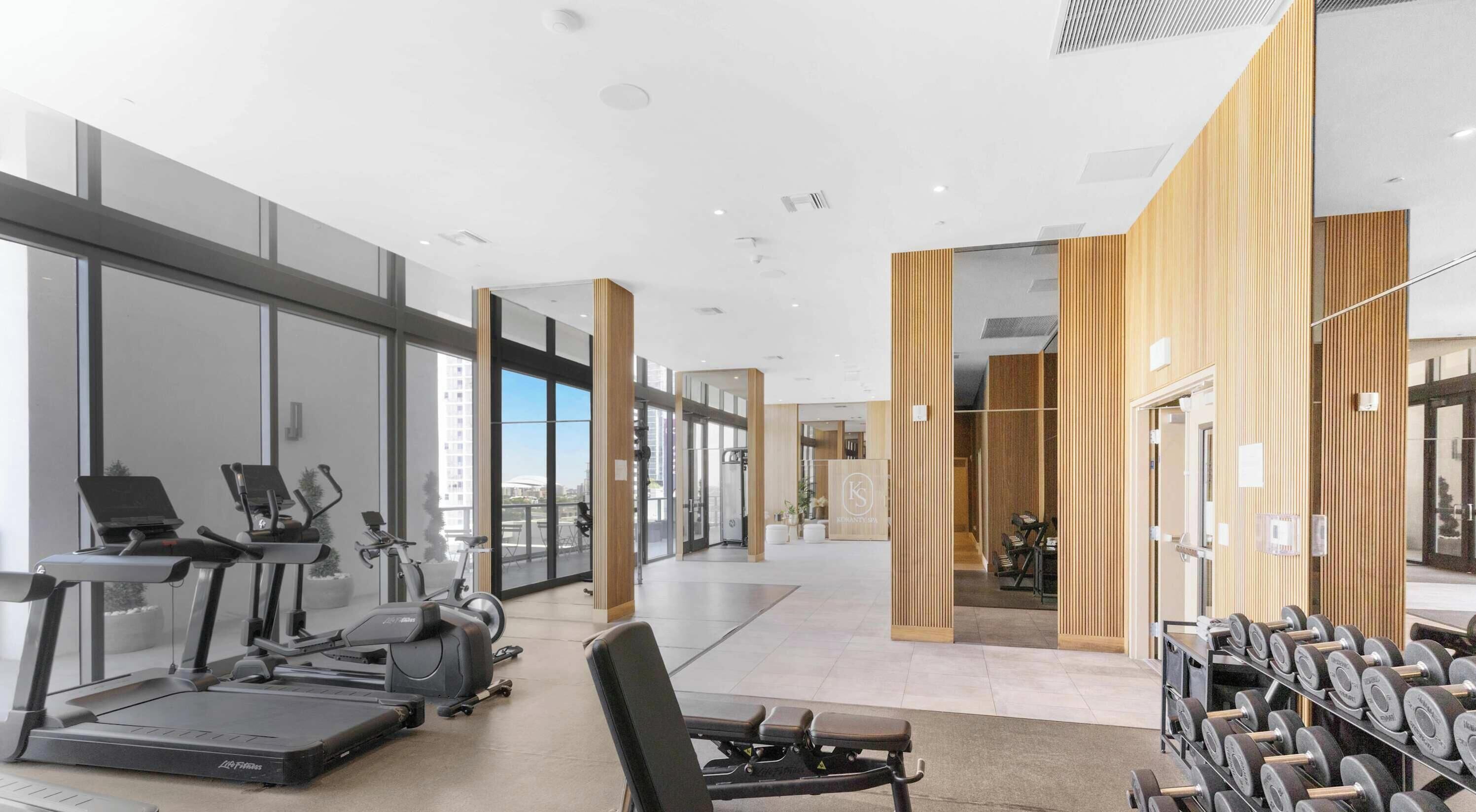 Un gimnasio moderno con equipo de ejercicio, ventanas amplias y vistas de la ciudad.