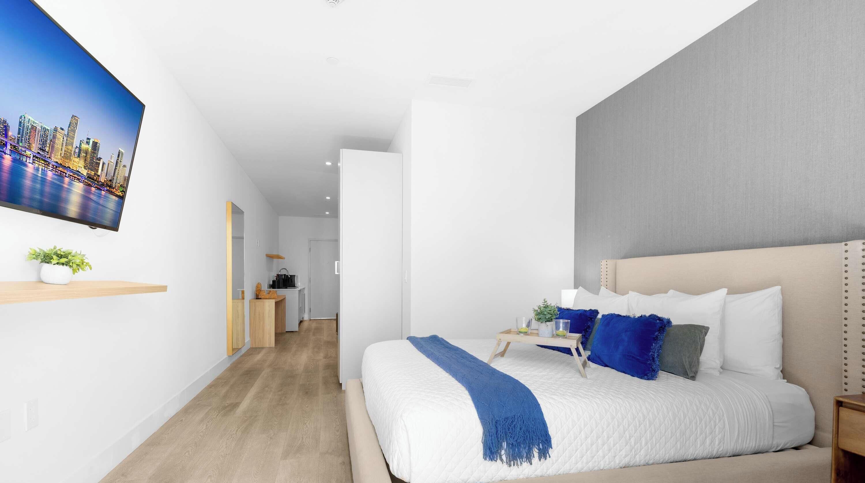 Una habitación de hotel moderna con una cama grande, un televisor en la pared y vistas a un paisaje urbano.