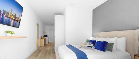 Una habitación de hotel moderna con una cama grande, un televisor en la pared y vistas a un paisaje urbano.