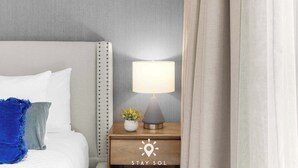 Een keurig opgemaakt bed met kussens, een bedlampje en een kleine plant op een houten nachtkastje.