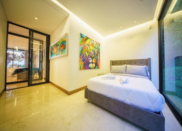A modern bedroom with a large bed, a glass door leading to a balcony, and two vibrant paintings on the walls.