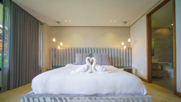 Una cama grande con cabecera, dos almohadas y dos toallas con forma de cisne sobre la cama.