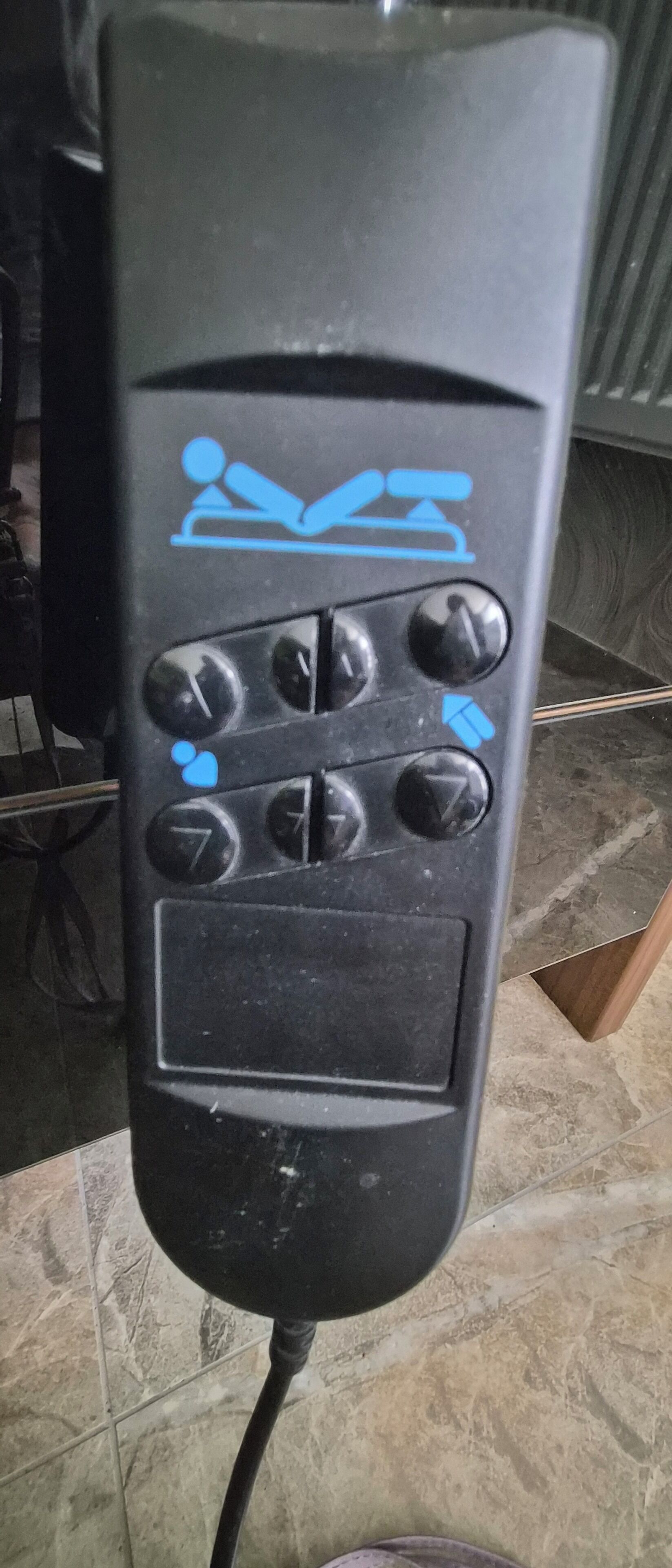 Une télécommande noire avec une icône bleue représentant une personne allongée, plusieurs boutons directionnels et un petit écran.