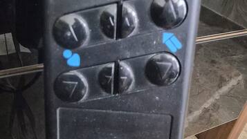 Une télécommande noire avec une icône bleue représentant une personne allongée, plusieurs boutons directionnels et un petit écran.