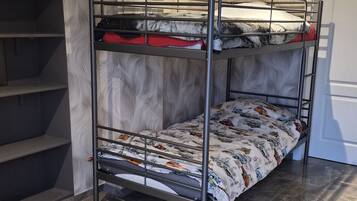 Un lit superposé avec une couvre-lit à motifs, une étagère et un sol carrelé en marbre, dans une pièce aux murs texturés.