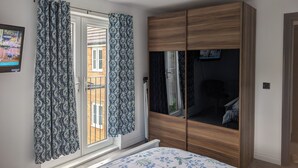 Un dormitorio con cama, armario, televisor y ventana con cortinas.