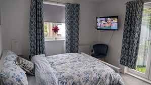 Un dormitorio con cama, una silla, un televisor y una ventana con cortinas.