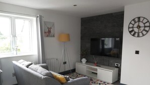Una sala de estar moderna con un sofá gris, un televisor de pantalla plana montado en una pared oscura y un reloj decorativo.