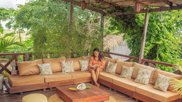 Una terraza de madera con un amplio sofá modular, un taburete tejido y una mesa de centro de madera.