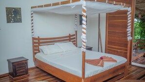 Una cama con dosel de madera, una mesita de noche pequeña y un tapete redondo tejido en el suelo.