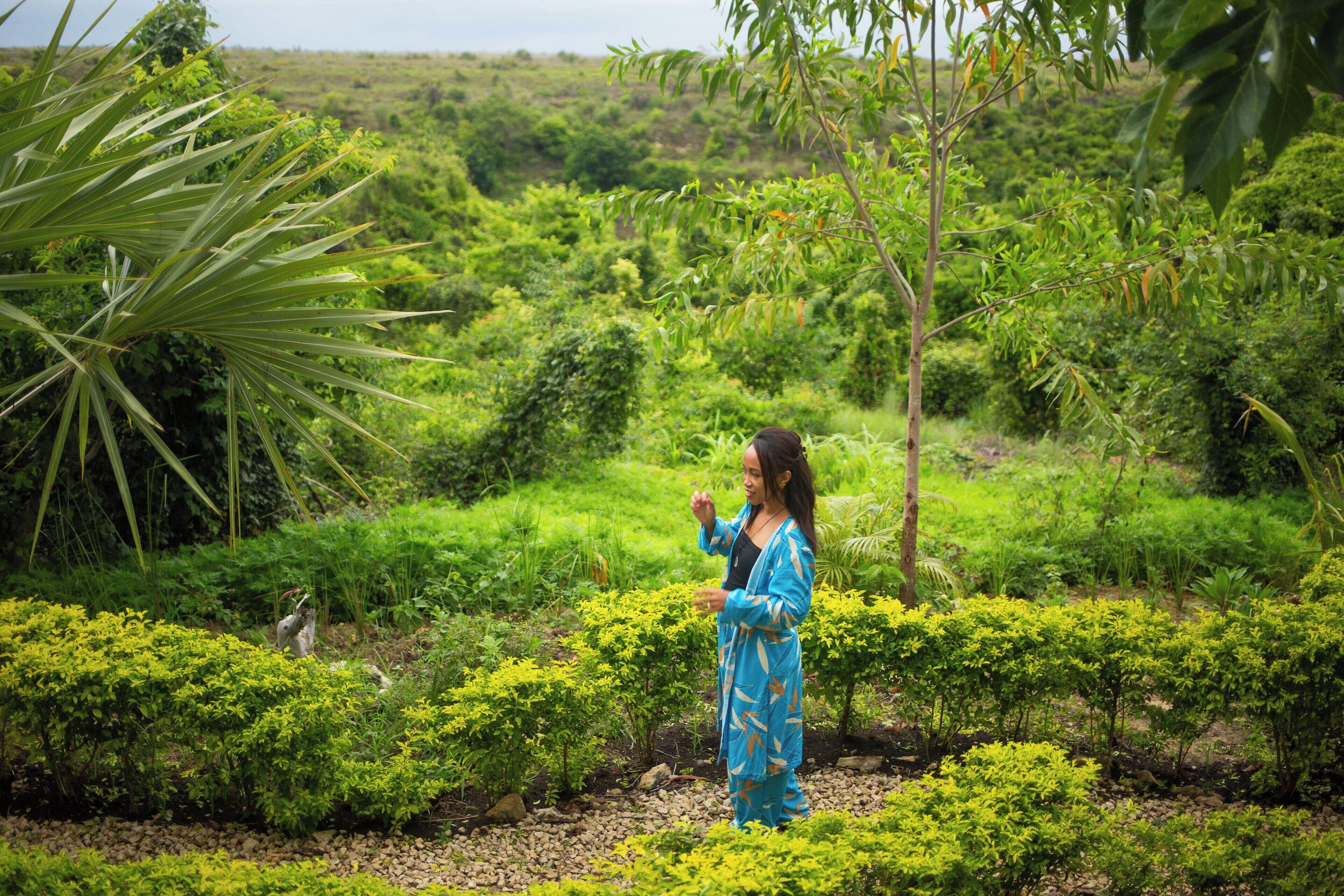 A person standing in a lush garden with dense greenery and a variety of plants.