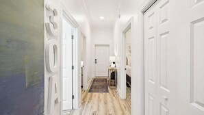 Ein Flur mit weißen Türen, Holzboden und einem Teppich, der zu einem Zimmer mit einem Bett und einer Lampe führt.
