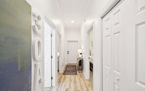 Ein Flur mit weißen Türen, Holzboden und einem Teppich, der zu einem Zimmer mit einem Bett und einer Lampe führt.