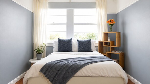A bedroom with a bed, two pillows, a bedside table, a plant, a window with curtains, and a wooden shelf with books. - OVERSIZED, CONTEMPORARY & CHARMING-GREAT VALUE!3min train to CBD/Shared Parking. (Darlinghurst)