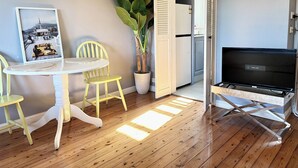 A compact living space with a dining table, chairs, a potted plant, a refrigerator, and a television. - OVERSIZED, CONTEMPORARY & CHARMING-GREAT VALUE!3min train to CBD/Shared Parking. (Darlinghurst)