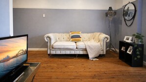 A living room with a sofa, a television, a floor lamp, and a wall-mounted mirror. - OVERSIZED, CONTEMPORARY & CHARMING-GREAT VALUE!3min train to CBD/Shared Parking. (Darlinghurst)