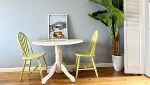 A room with a round white table, two green chairs, a framed picture on the table, and a large potted plant. - OVERSIZED, CONTEMPORARY & CHARMING-GREAT VALUE!3min train to CBD/Shared Parking. (Darlinghurst)