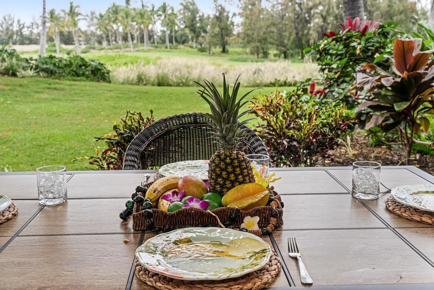 A table set outdoors with a pineapple centerpiece, fruits, and glasses.