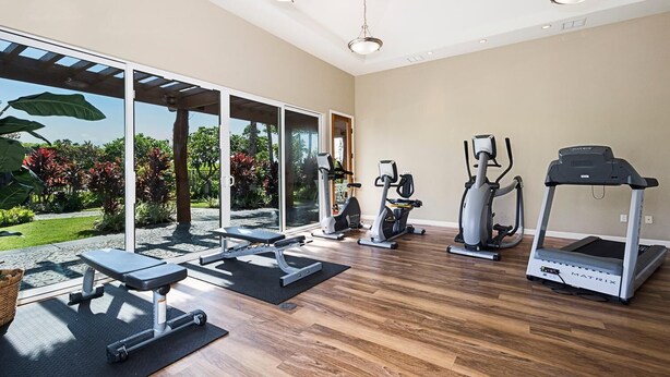 Un gimnasio en casa con equipo de ejercicio, ventanas amplias y vistas a un jardín.