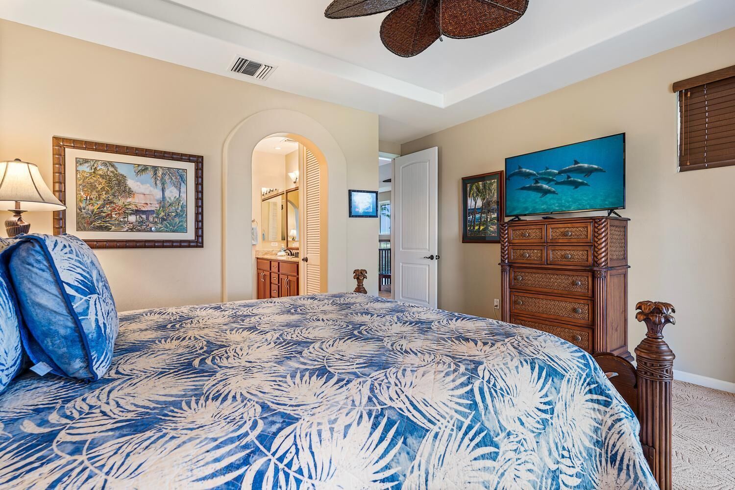 A bedroom with a large bed, a dresser, a television, and a painting of dolphins.