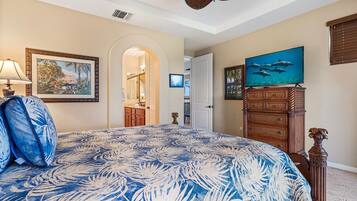 A bedroom with a large bed, a dresser, a television, and a painting of dolphins.