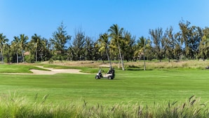 Un campo de golf con un carrito de golf, búnkeres de arena y palmeras.