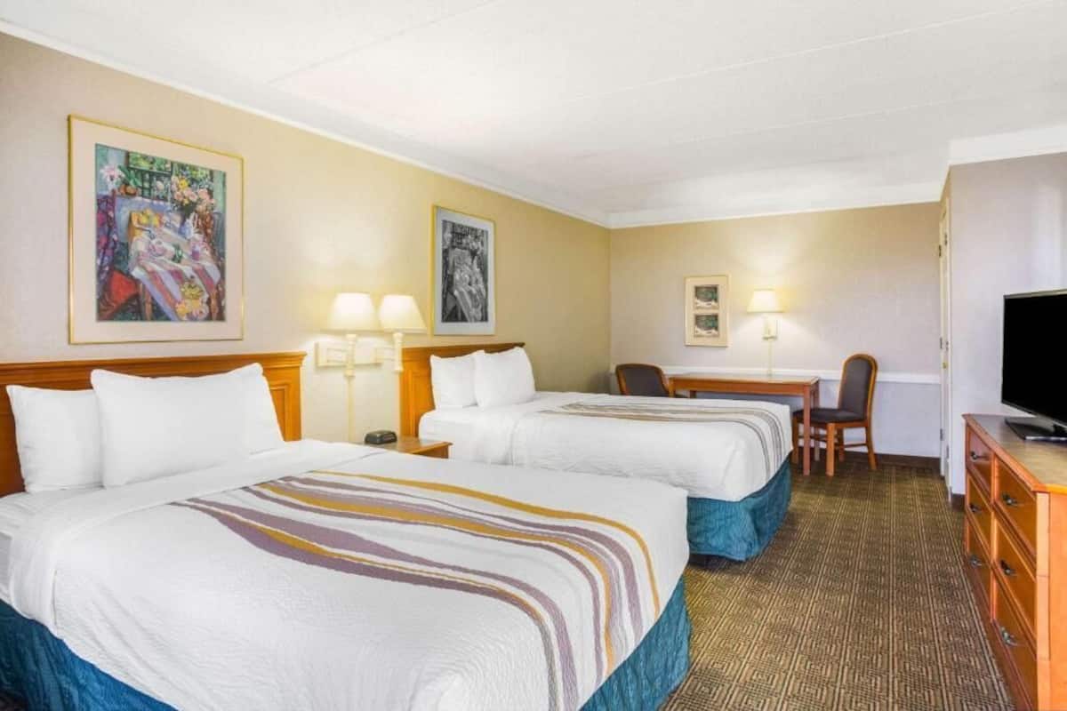A hotel room with two beds, a desk, a chair, a television, and artwork on the walls.
