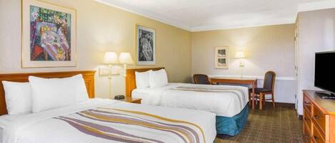 Une chambre d’hôtel avec deux lits, un bureau, une chaise, une télévision et des œuvres d’art accrochées aux murs.